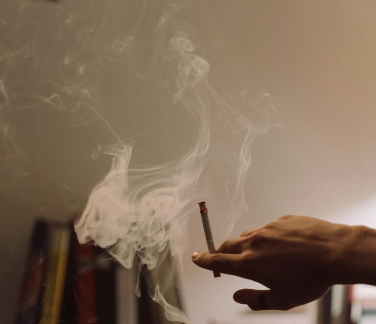 A man lies indoors, blowing smoke, creating a relaxed, moody atmosphere.